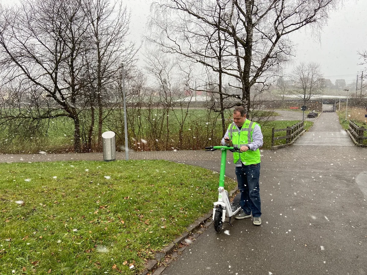 Mathias Niederberger schaut auf seine App. Er steht neben einem Lime-Fahrzeug.
